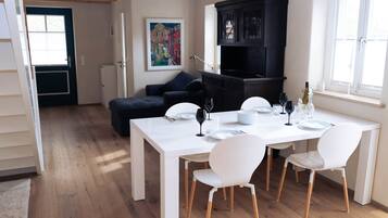 A dining area with a white table set for six, surrounded by white chairs. A black cabinet is against the wall, and a colorful painting hangs above the table.