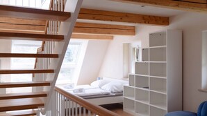 A modern bedroom with a wooden staircase, a bed with white linens, and a blue chair. - Remark Studios: Historic and modern Apartment (Burgwedel)