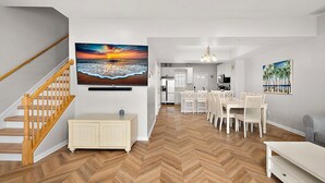 Eine moderne Küche mit weißen Schränken, ein Essbereich mit weißen Stühlen und ein Fischgrätenparkettboden.