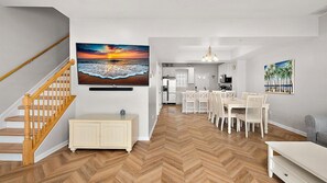 A modern kitchen with white cabinets, a dining area with white chairs, and a herringbone wood floor. - Steps to the Sand & Boardwalk! Spacious 4BR Downtown OC Townhouse, Sleeps 12 (Ocean City)