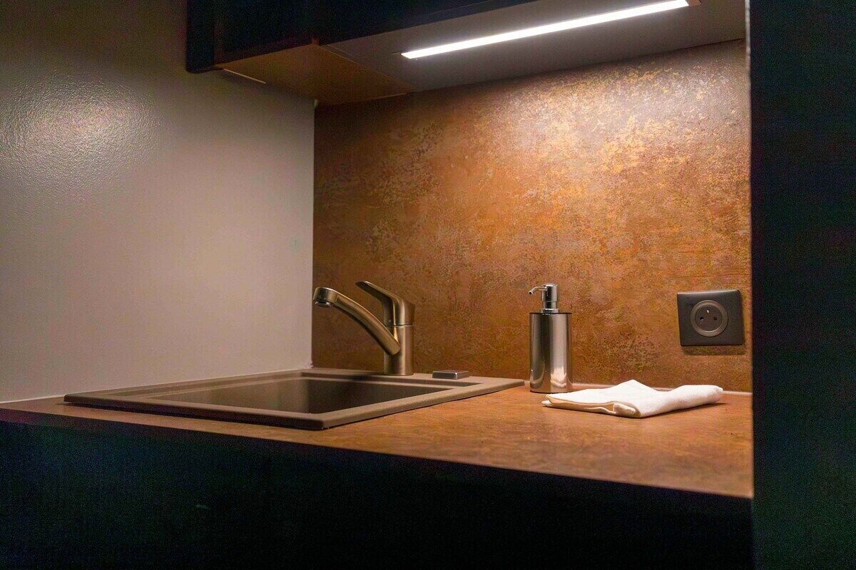 A modern kitchen with a stainless steel sink, a faucet, a soap dispenser, and a towel on the counter.