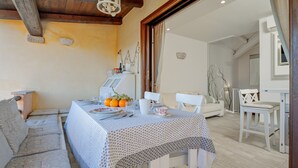 A dining area with a table set for two, a sofa, and a white chair. - Villetta 'Sky View' with Sea View, Wi-Fi, and Air Conditioning (Golfo Aranci)