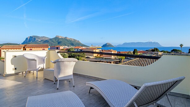 A rooftop terrace with wicker furniture, a view of the sea, and buildings in the background. - Villetta 'Sky View' with Sea View, Wi-Fi, and Air Conditioning (Golfo Aranci)