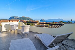 A rooftop terrace with wicker furniture, a view of the sea, and buildings in the background. - Villetta 'Sky View' with Sea View, Wi-Fi, and Air Conditioning (Golfo Aranci)