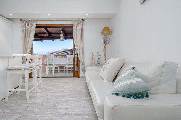 Une pièce avec un canapé blanc, une table à manger avec des chaises, une lampe et une vue sur un immeuble par la fenêtre.