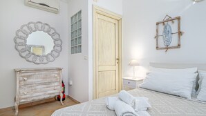 A bedroom with a bed, a dresser, a mirror, a door, and a wall decoration. - Villetta 'Sky View' with Sea View, Wi-Fi, and Air Conditioning (Golfo Aranci)