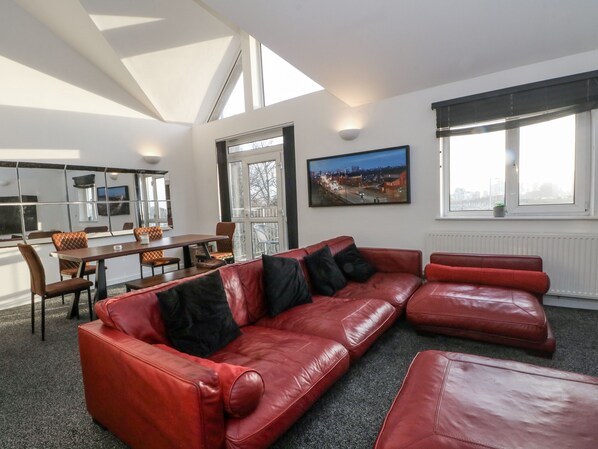 Ein modernes Wohnzimmer mit einem roten Ledersofa, einem Essbereich mit Tisch und Stühlen sowie einem Stadtbildgemälde an der Wand.
