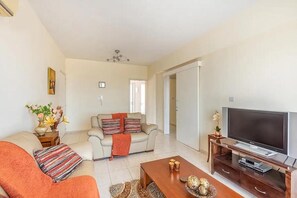 A living room with a sofa, a coffee table, a TV, and a door leading to another room. - Modern stylish 2 bedroom apartment with communal pool in Neo Chorio Village (Neyohoryo Baf)