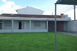 A modern building with a flat roof, a covered patio area, and a well-maintained lawn. - Luxury Spacious House up to 09 People on Guaritá Street (Fazenda Rio Grande)