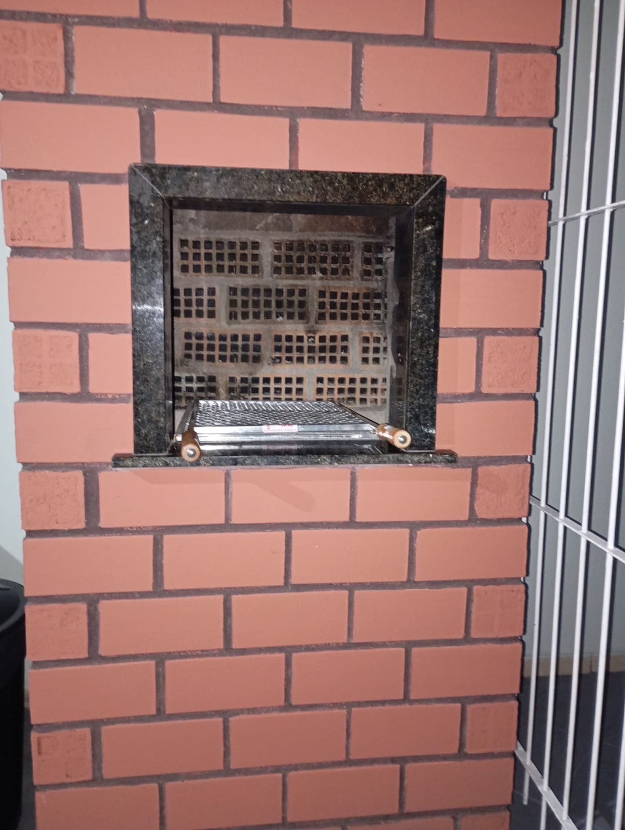 Un muro de ladrillo con una celosía metálica y un pequeño estante.
