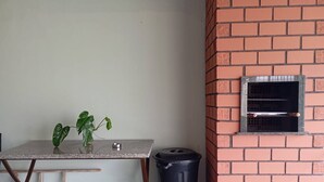 Een kamer met een tafel, een kamerplant, een afvalbak en een bakstenen muur met een raam.