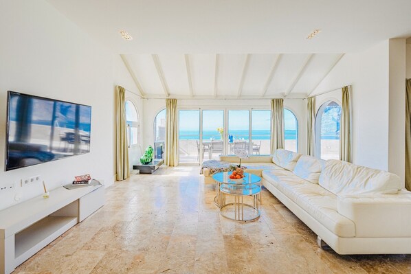 Un salon spacieux doté d’un grand téléviseur, d’un canapé, d’une table basse et offrant une vue sur la mer grâce à de grandes fenêtres.
