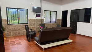 A room with a sofa, chairs, a TV, and a stone wall. - Country Cabin With Mountain Views (San Gil)