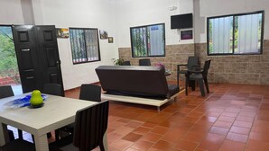 A spacious living area with a sofa, dining table, and chairs. There are windows with curtains, a television, and a door. - Country Cabin With Mountain Views (San Gil)