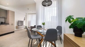 Een moderne eetruimte met een glazen tafel, grijs beklede stoelen en een houten buffetkast.
