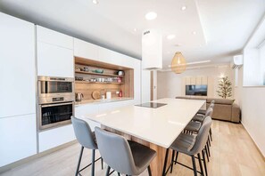 Een moderne keuken met witte kasten, een ingebouwde oven en een groot kookeiland met barkrukken.