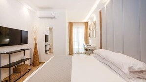 Ein modernes Hotelzimmer mit Flachbildfernseher, einem Nachttisch mit Vase, einem Bett mit weißer Bettwäsche, einem Schreibtisch mit Stuhl und einem großen Fenster mit Vorhängen.