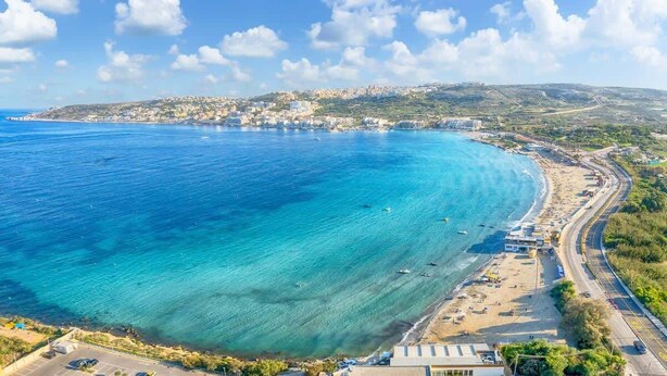 Eine Küstenstadt mit blauem Meer, einem Strand und einer parallel zur Küste verlaufenden Straße.