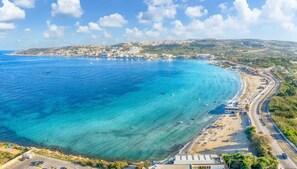 Eine Küstenstadt mit blauem Meer, einem Strand und einer parallel zur Küste verlaufenden Straße.