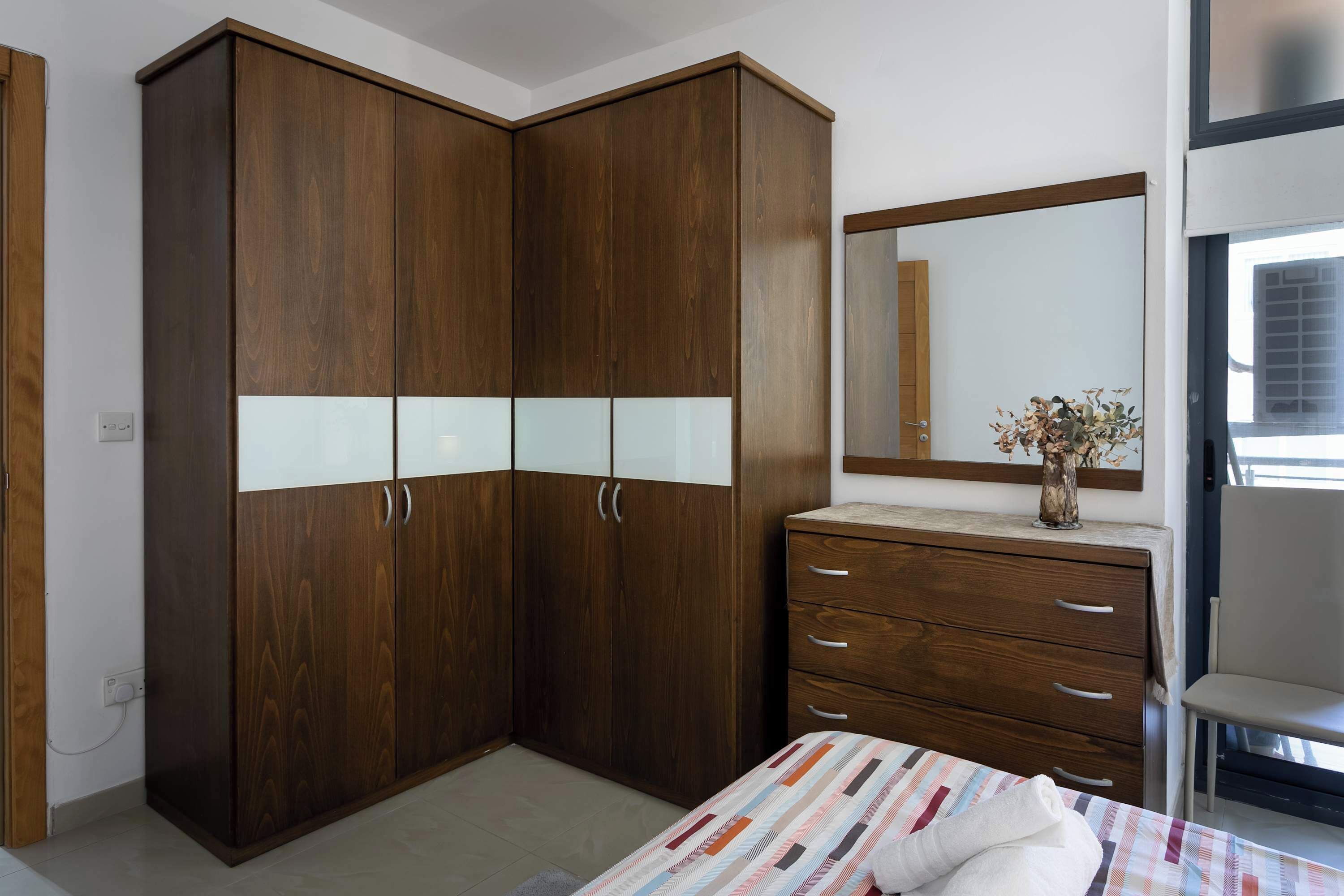 Une chambre à coucher avec une grande armoire, un lit recouvert d’une courtepointe à rayures, une commode et un miroir.