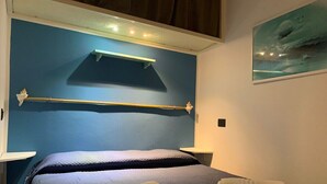 Un lit double avec des serviettes pliées, une tête de lit dotée d’une étagère, des tables de chevet et un tableau accroché au mur.