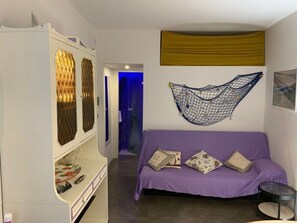 A room with a purple sofa, a white cabinet with glass doors, a hammock, and a small round table. - The Captain's Lair (Alghero)