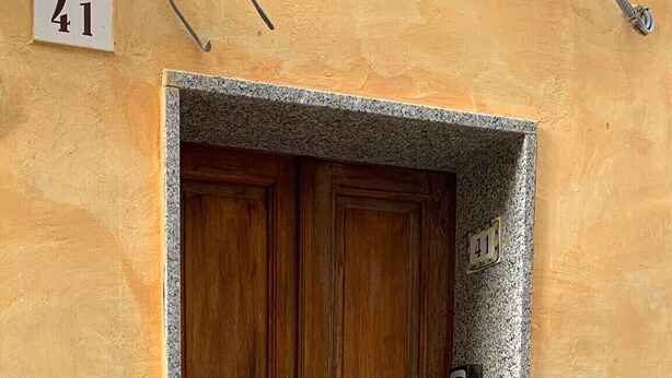 Une porte à double battant en bois, surmontée d’une petite corniche en pierre, avec une sonnette métallique et un panneau portant le numéro « 41 » fixé au mur.
