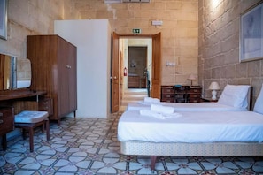 Habitación de hotel con cama, escritorio, armario y baño visible a través de una puerta abierta.