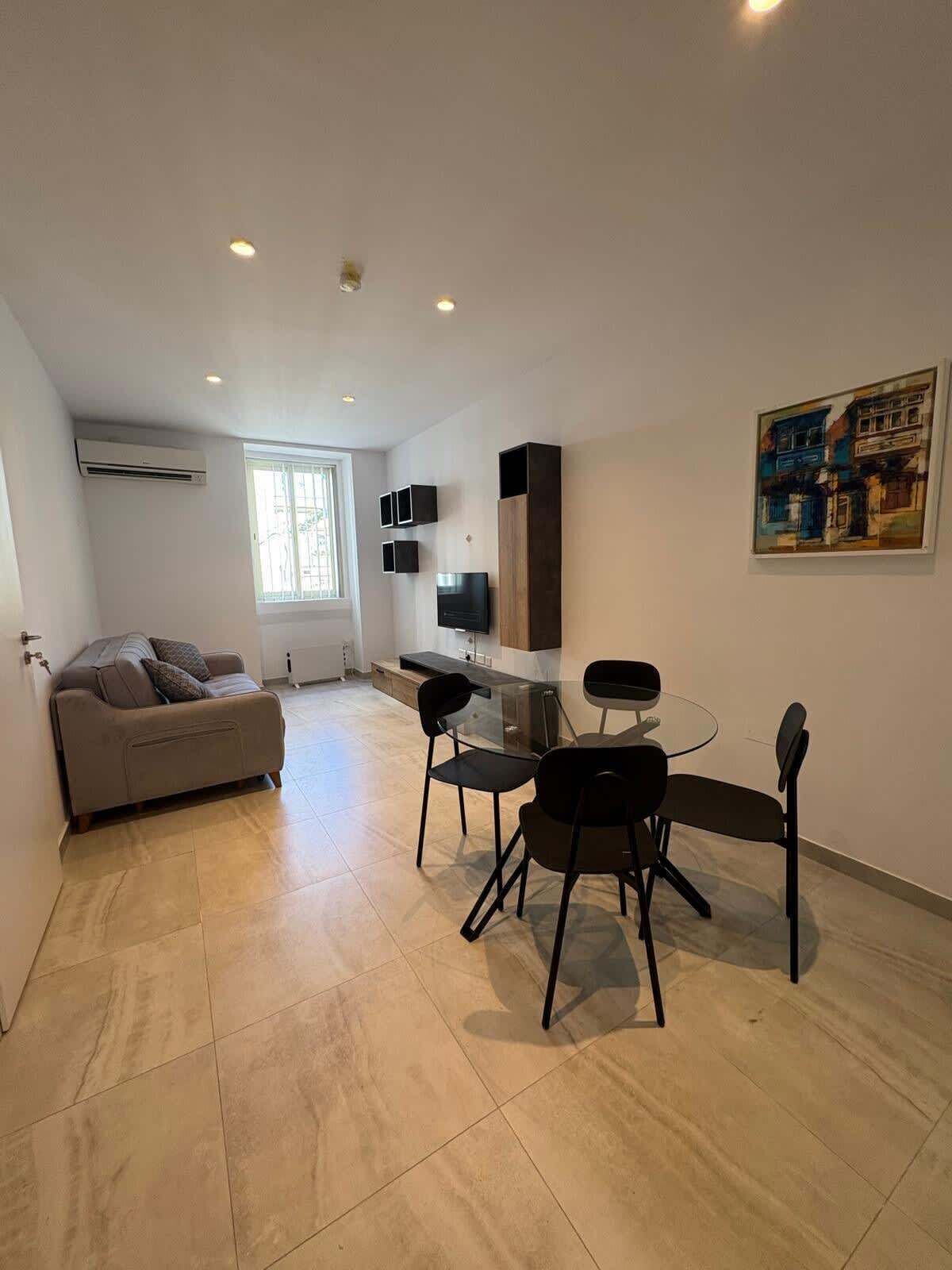 Un salon moderne avec un canapé, une table à manger et des chaises, un téléviseur et des œuvres d’art accrochées au mur.