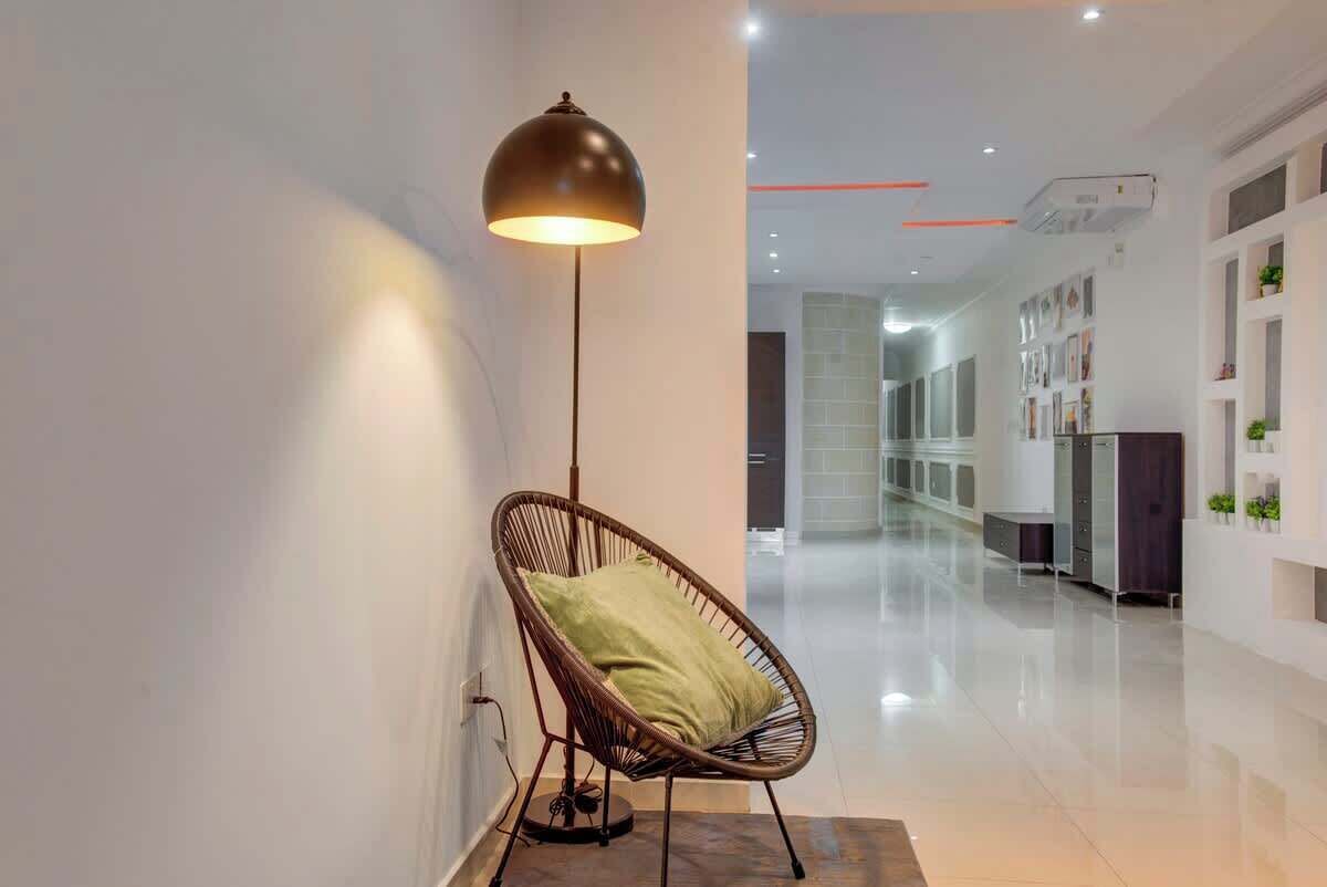 Ein modernes Interieur mit einer Stehlampe, einem Korbstuhl mit Kissen und einem Flur, der zu einem Raum mit großem Fenster führt.
