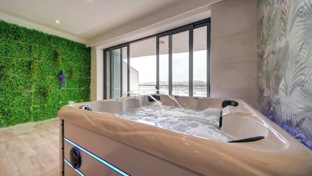 A hot tub with a view of a cityscape through large windows, a green wall, and a tiled floor. - Sliema 3BDR Flat with Seaview and Jacuzzi (Tas-Sliema)