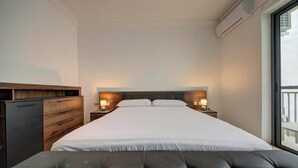 A modern hotel room with a large bed, bedside lamps, a wooden headboard, a grey upholstered bench, and a large window with a balcony view. - Sliema 3BDR Flat with Seaview and Jacuzzi (Tas-Sliema)