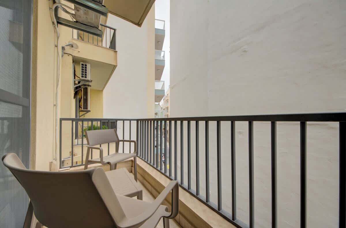 Un balcone con due sedie e un tavolo, affacciato su una strada con edifici.