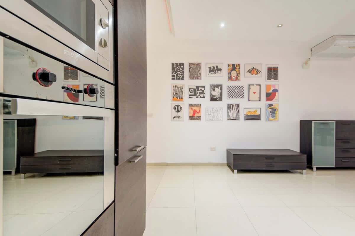 A modern room with a large cabinet, a bed, a small table, and a wall with various framed artworks.