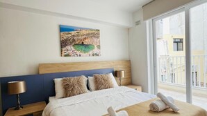 Et moderne hotelværelse med en stor seng, en sengegavl, et natbord, en lampe, et billede på væggen og udsigt fra vinduet.