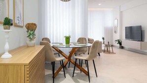 A modern dining area with a round glass table, beige chairs, and a wooden sideboard. - Shoreline Residence Brand NEW 1 BDR Apartment (Kalkara)