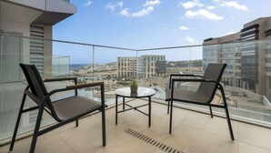A balcony with two chairs and a small table, overlooking a cityscape with modern buildings and a clear sky. - Shoreline Residence Brand NEW 1 BDR Apartment (Kalkara)