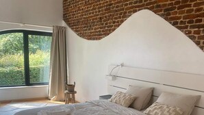A modern bedroom with a large bed, a brick wall, and a view of greenery. - Self-catering cottage with year-round heated indoor swimming pool (Ramillies)
