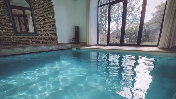 An indoor swimming pool with clear water, a brick wall, and large windows. - Self-catering cottage with year-round heated indoor swimming pool (Ramillies)