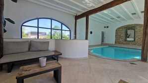 A pool area with a curved glass wall, a wooden bench, and a cushioned seating area with a view of the pool. - Self-catering cottage with year-round heated indoor swimming pool (Ramillies)