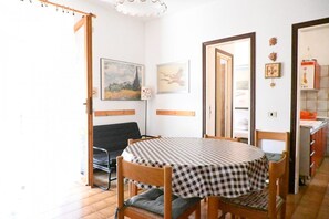 Un coin repas avec une nappe à carreaux, des chaises en bois, un canapé noir et un tableau accroché au mur.