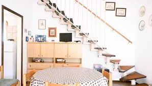 A dining area with a round table, chairs, a staircase, and a TV on a cabinet. - M444 - Marcelli, comfortable four-room apartment with outdoor patio (Marcelli)
