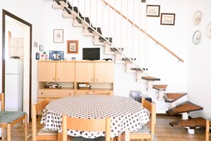Un coin repas avec une table ronde, des chaises, un escalier et un téléviseur posé sur un meuble.