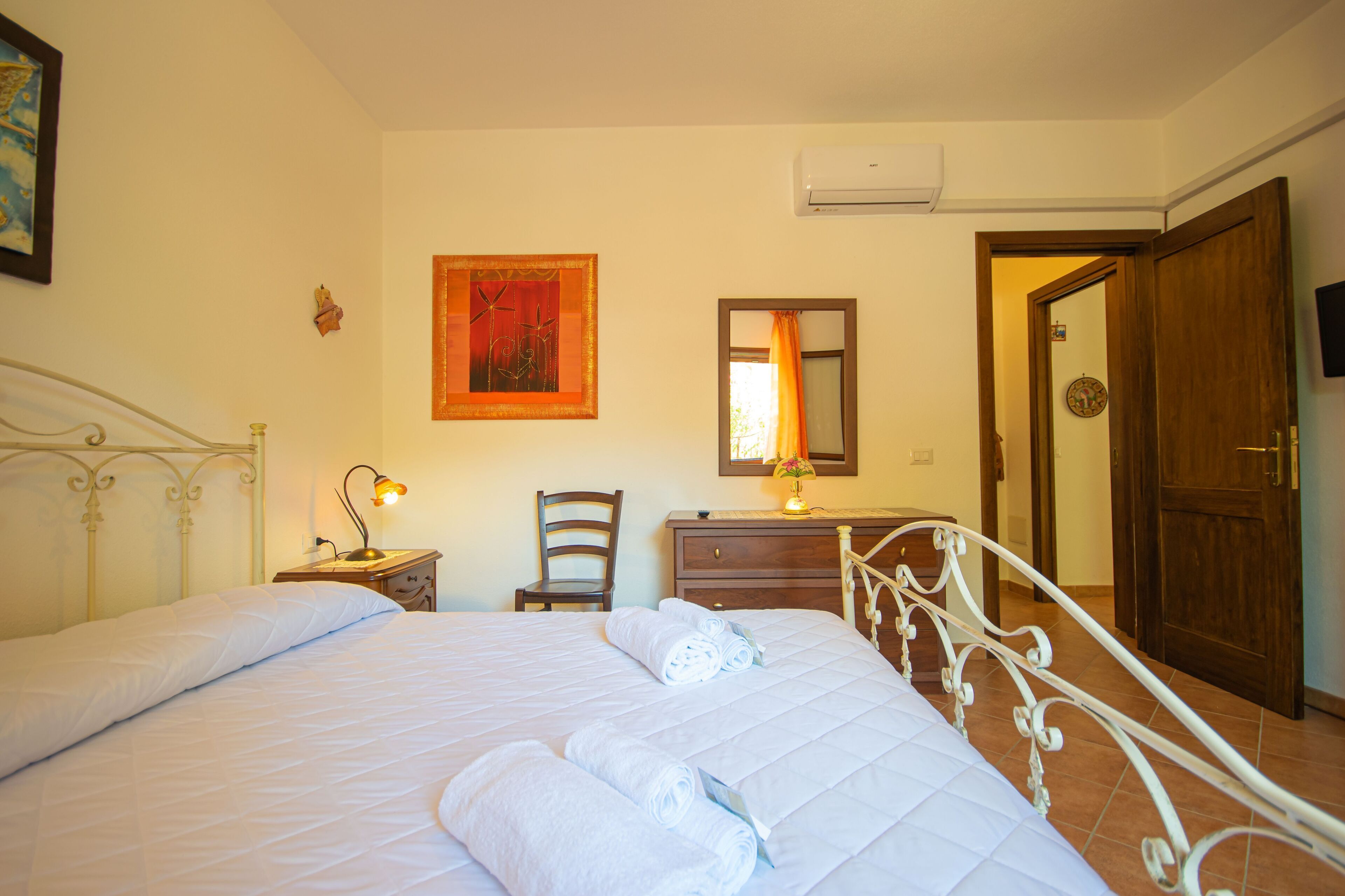 A neatly made bed with white linens, a bedside lamp, a chair, a dresser, and a mirror on the wall.