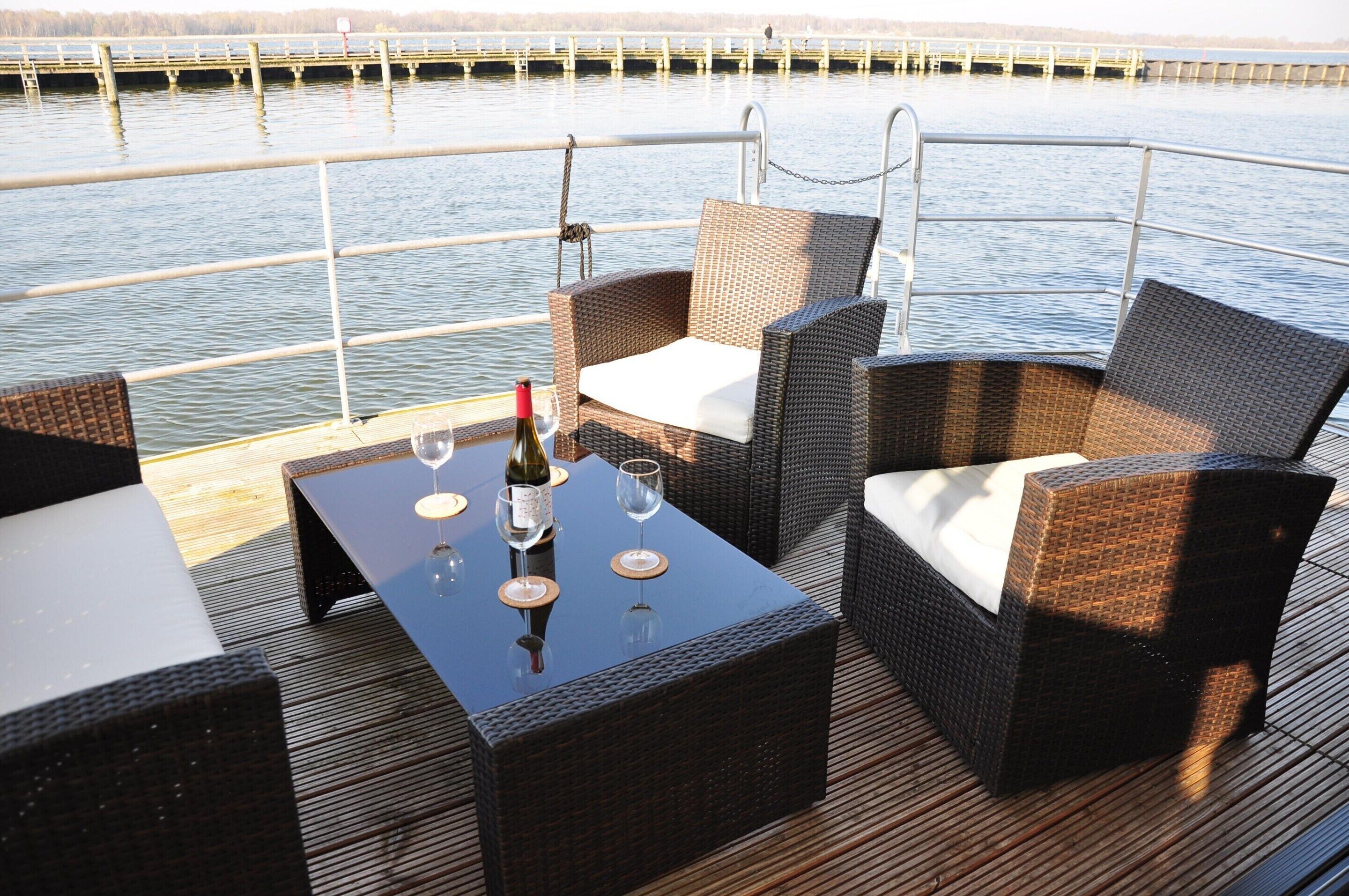 A deck with wicker furniture, a table with a bottle of wine, and glasses.