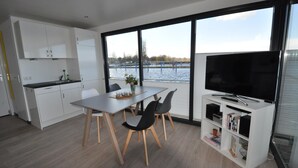 Eine moderne Küche mit weißen Schränken und einem Essbereich mit Tisch und Stühlen. Ein großes Fenster bietet Blick auf ein Gewässer.