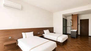 Habitación de hotel con dos camas, cabecero de madera, aire acondicionado integrado, baño con espejo y suelo con patrón de espiga.