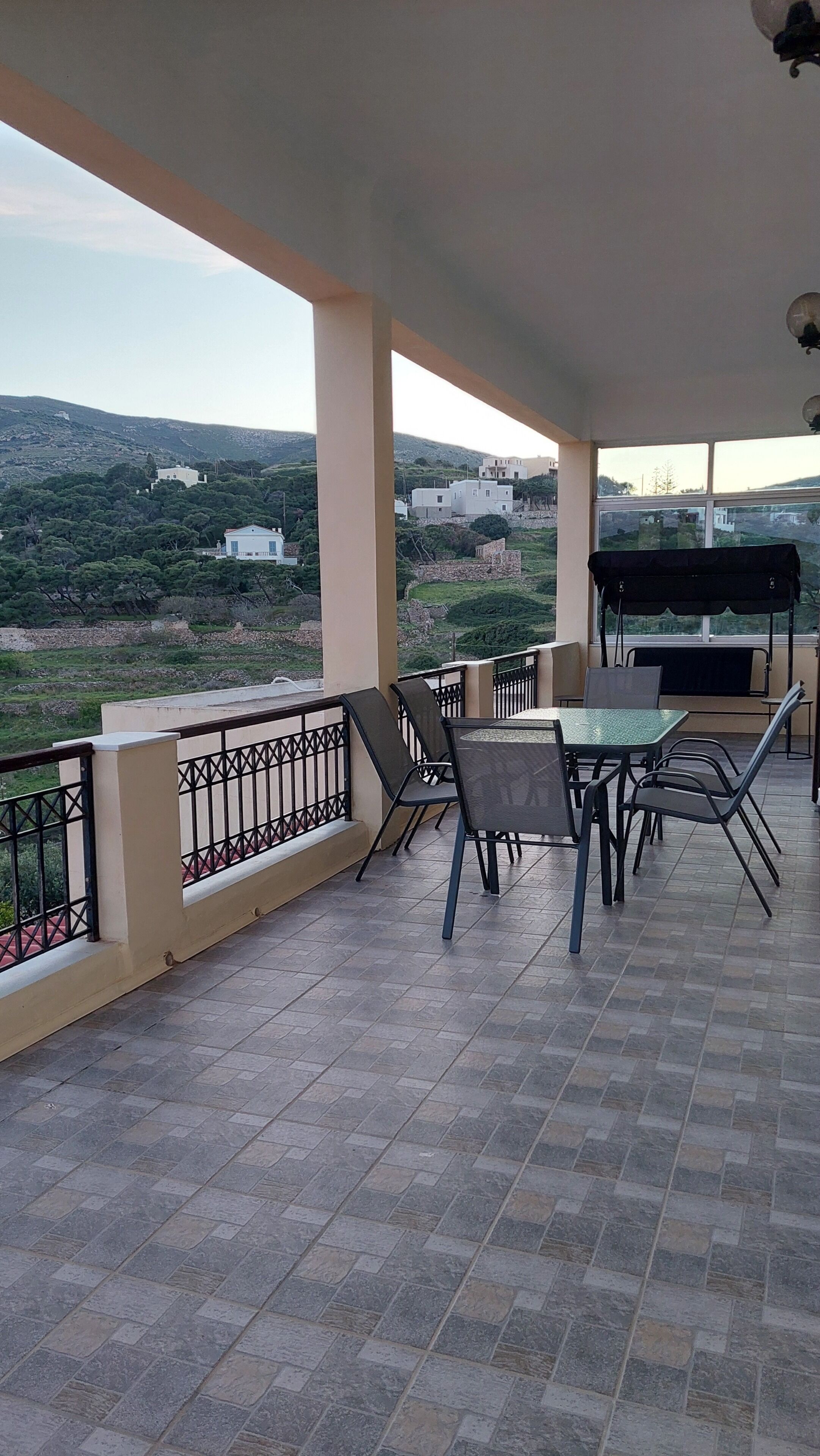 Une terrasse couverte avec une table et des chaises, un barbecue et une vue sur un paysage vallonné.