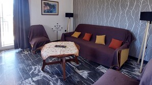 Un salon moderne avec un canapé, un pouf et deux fauteuils, un mur à motifs et un lustre.