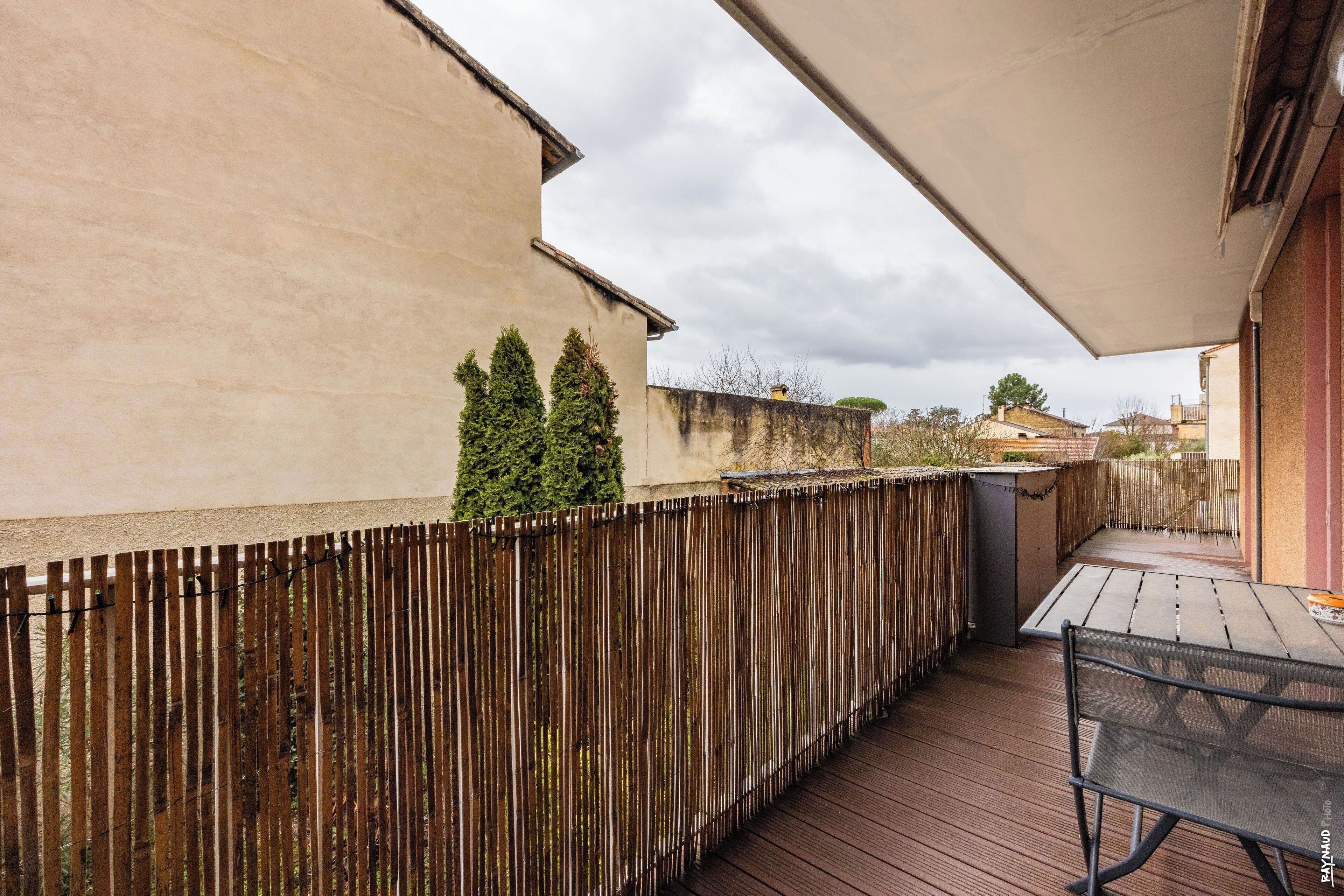 A wooden deck with a table and chairs, a wooden fence, and a building in the background.
